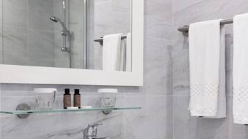 Un baño con un espejo grande, un lavabo y una repisa de vidrio con artículos de aseo.