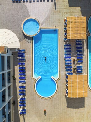 An aerial view of a swimming pool area with multiple pools and sun loungers arranged around it.