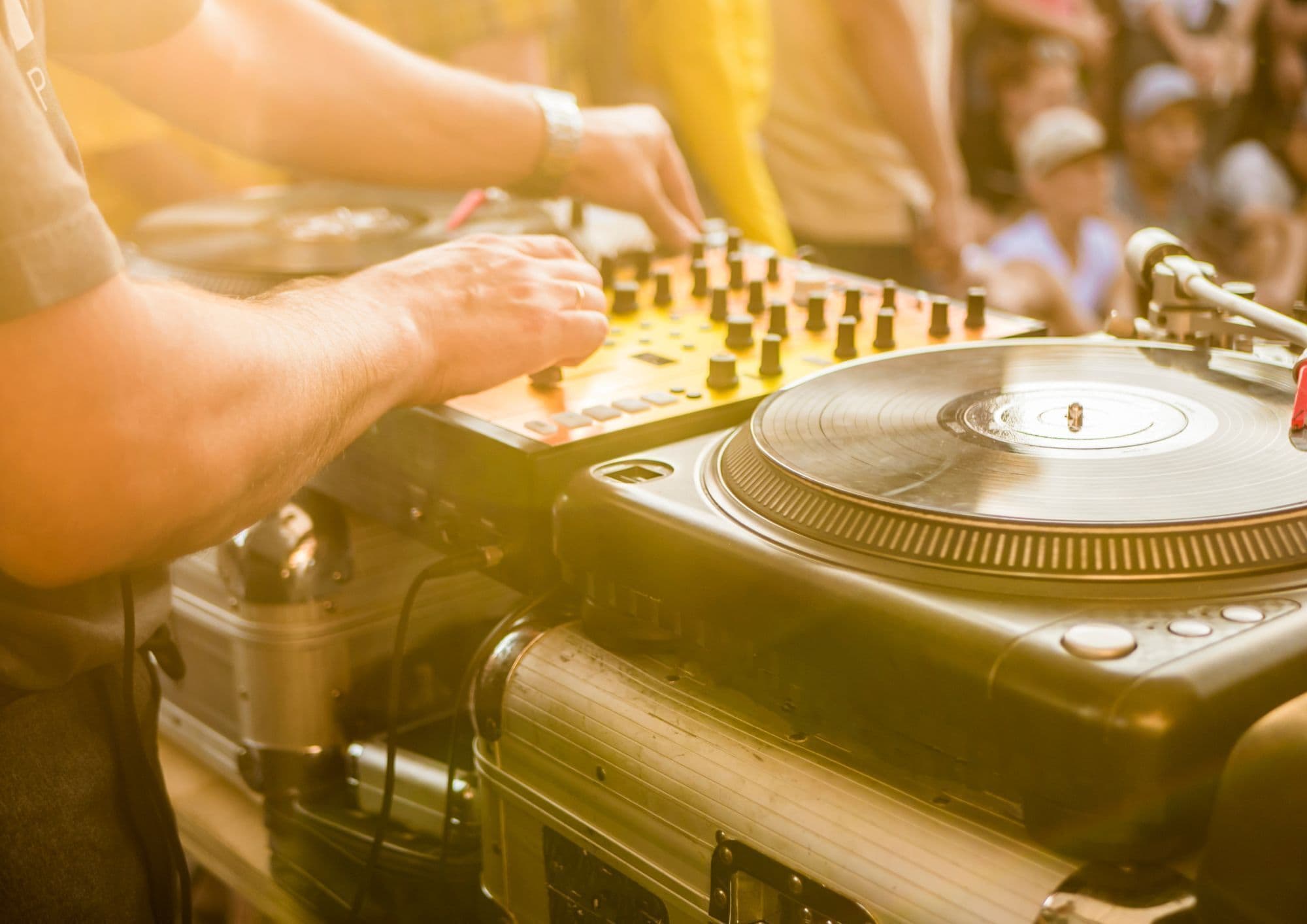 Primi piani delle mani di un DJ che manovrano un giradischi e un mixer.