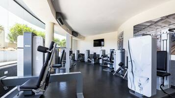 Une salle de sport moderne équipée de divers appareils d’exercice, dotée de grandes fenêtres et d’un plafond plat.