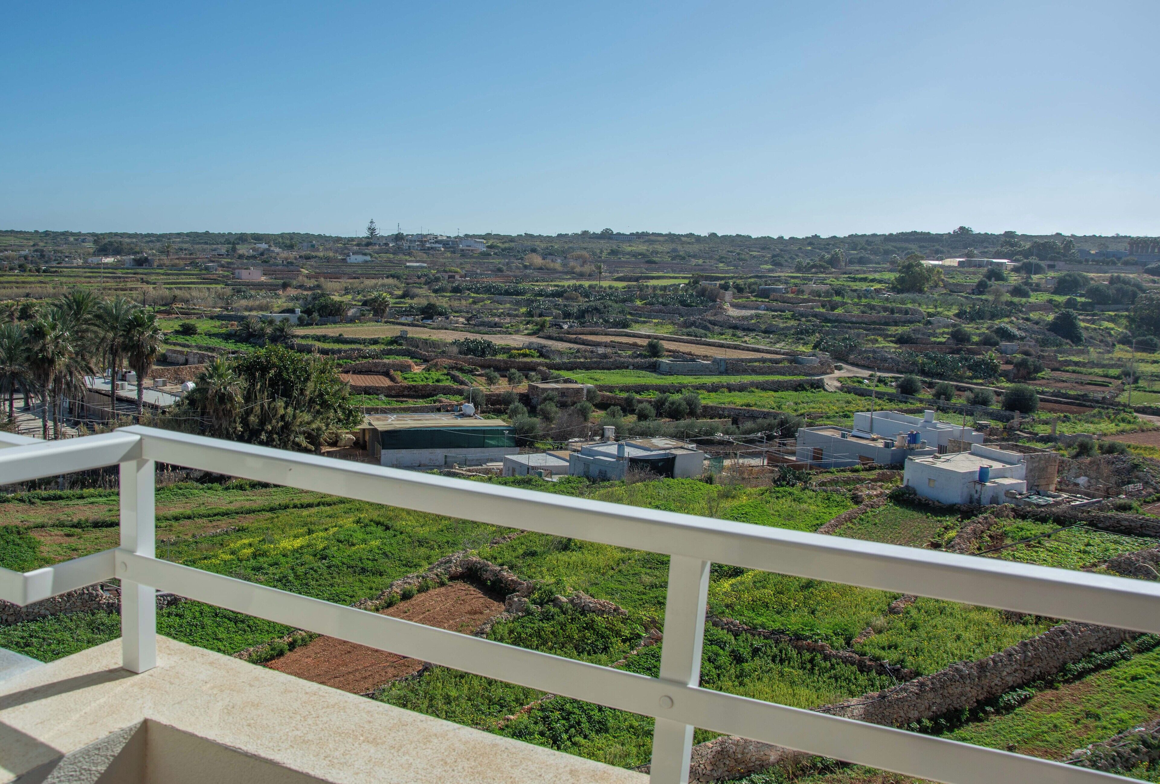 A balcony with a view of a rural landscape, including fields and scattered buildings.