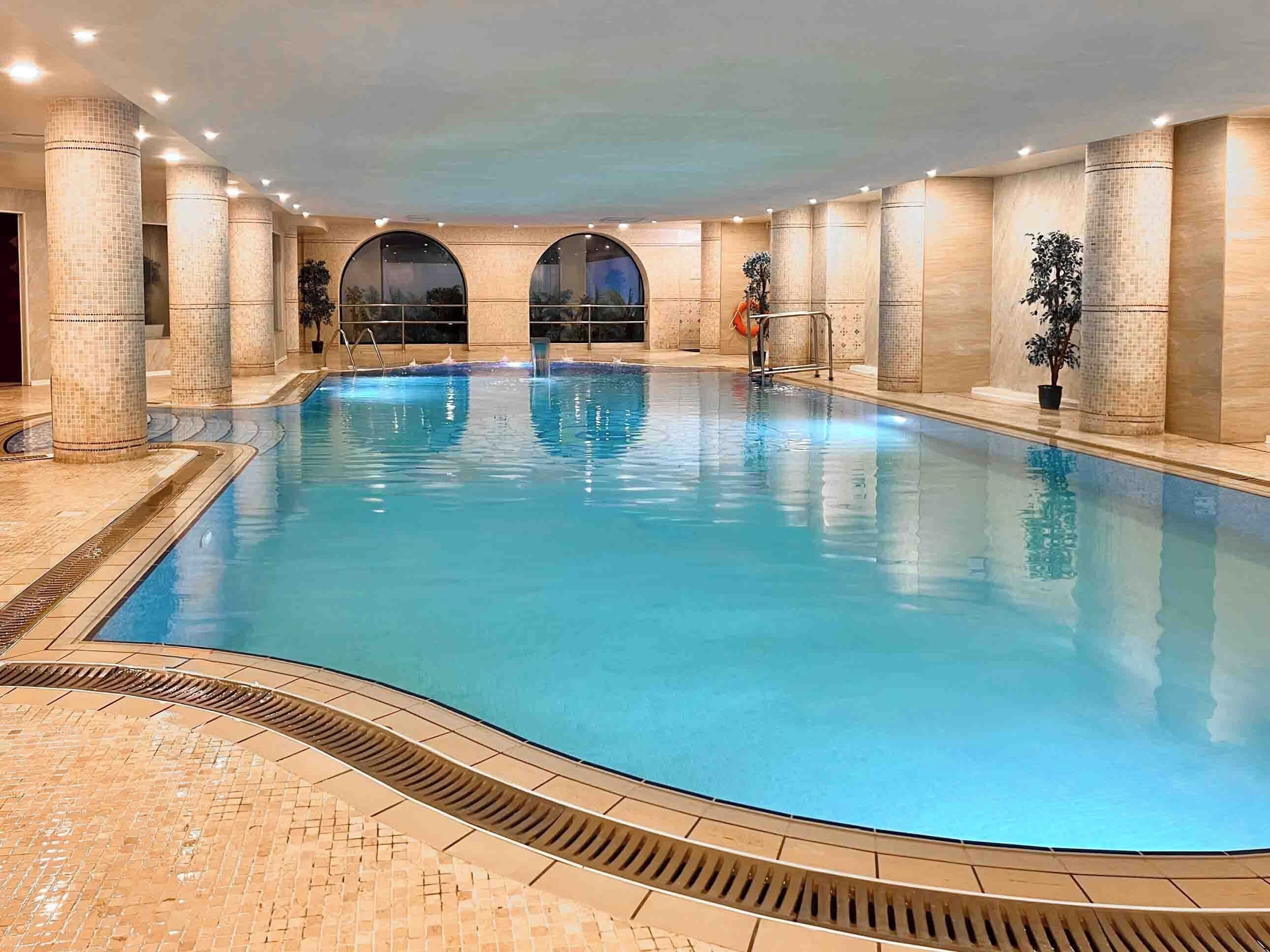 An indoor swimming pool with tiled walls and a tiled floor, surrounded by columns and arches.