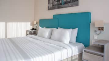 A hotel room with a bed, a nightstand with a phone, a wall-mounted lamp, and a painting above the bed.