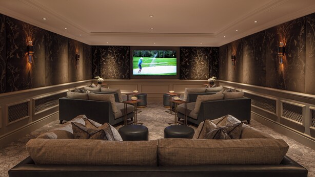 A spacious living room with a large flat-screen TV, comfortable seating, and decorative wall sconces. - Four Seasons Hotel Hampshire (Hook)