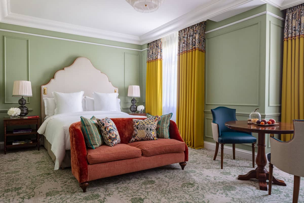A hotel room with a large bed, a red sofa, a round wooden table, and a blue chair.