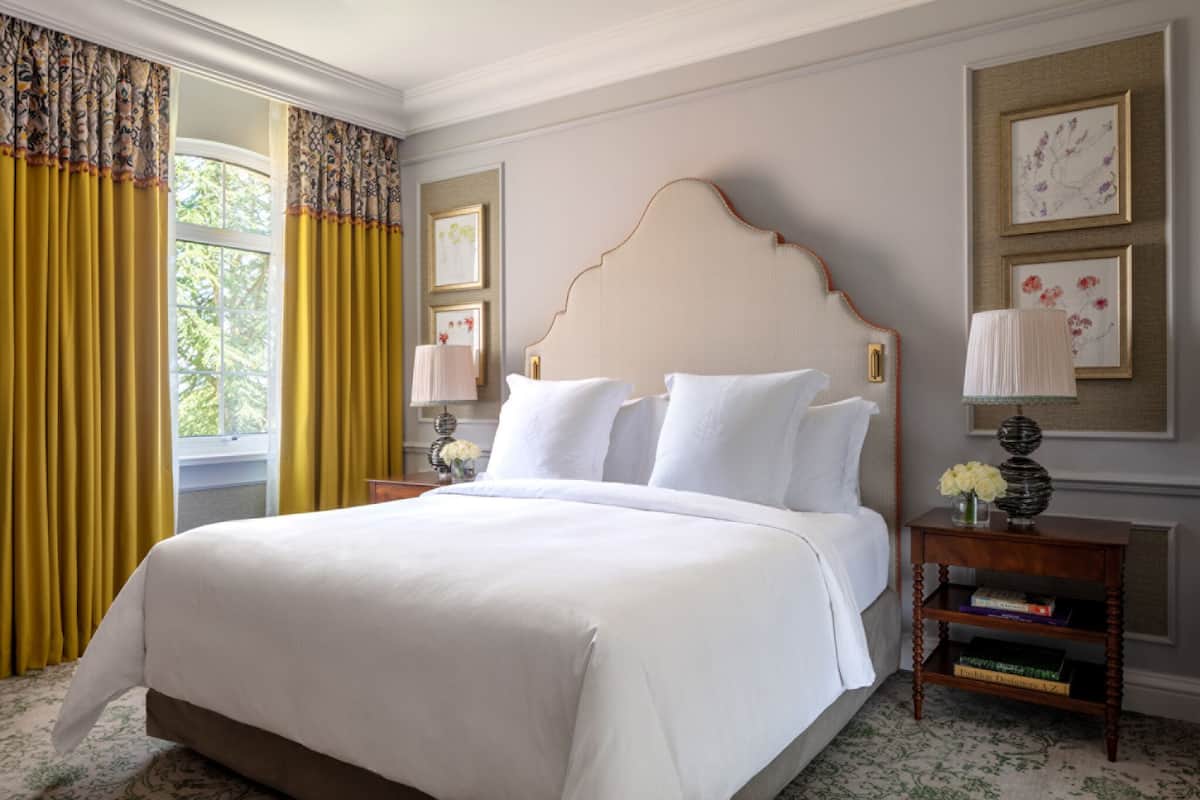 A neatly made bed with white linens, a wooden headboard, and a bedside table with a lamp and books.
