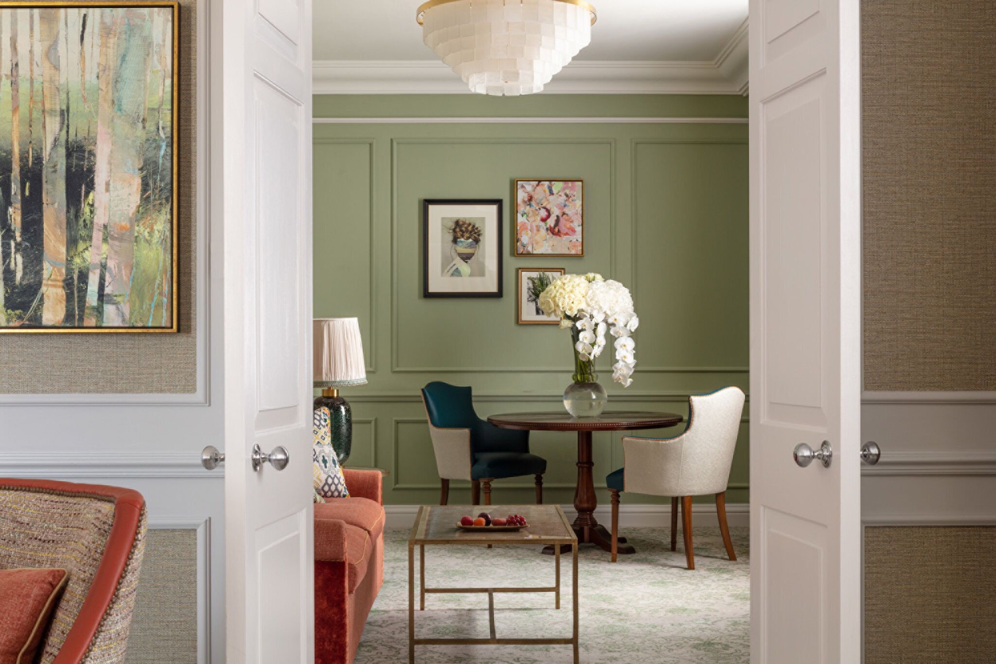A room with a green wall, a round dining table with chairs, a coffee table, and a door leading to another room.