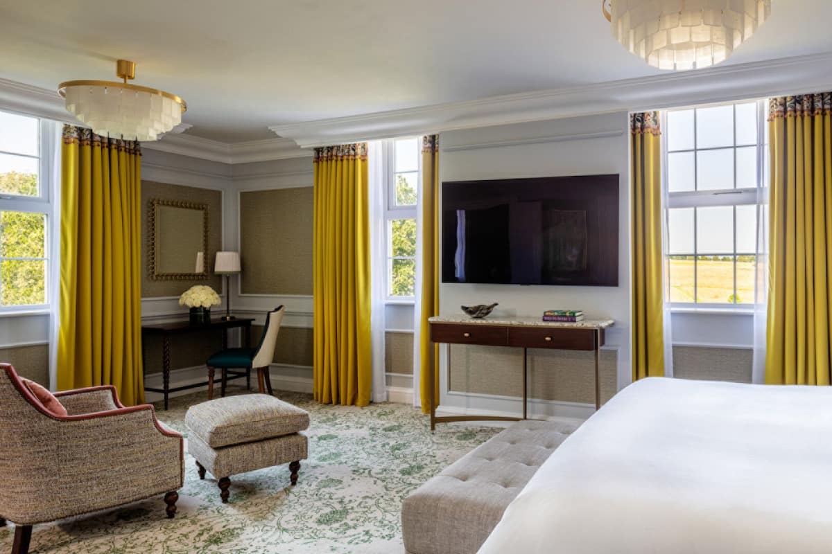 A hotel room with a large bed, a desk with a television, a chair, and a sofa.