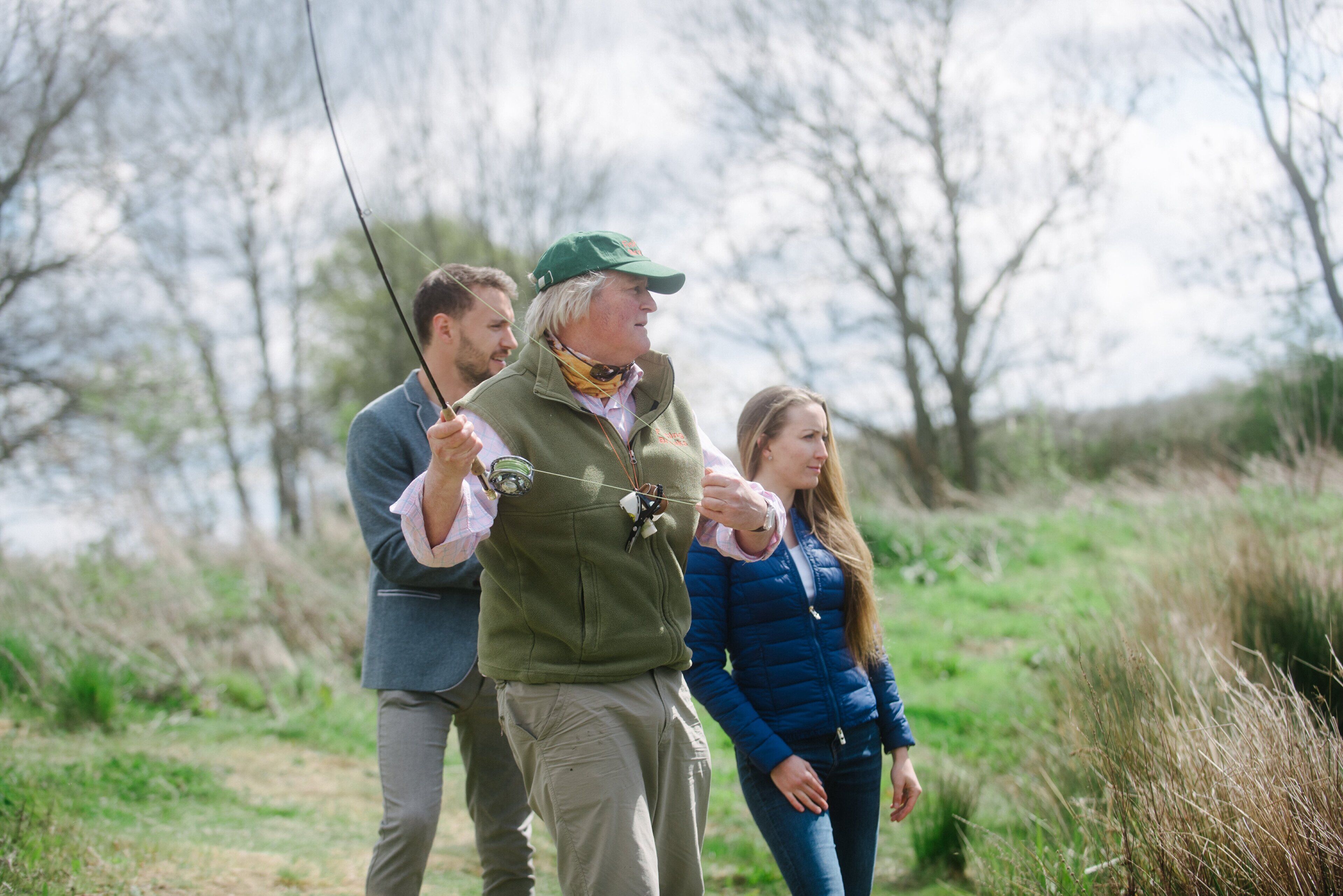 Three people outdoors, one holding a fishing rod.