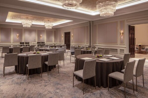 Un amplio salón de conferencias con mesas y sillas redondas, candelabros y suelo alfombrado.