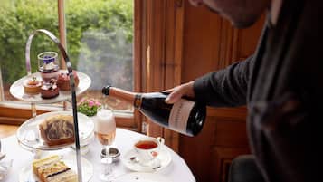 A person pouring a bottle of wine onto a table with a tiered dessert stand and a cup of tea.