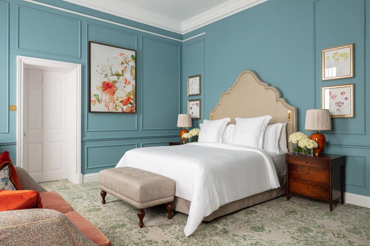 A bedroom with a large bed, a nightstand, a bench, and a door.
