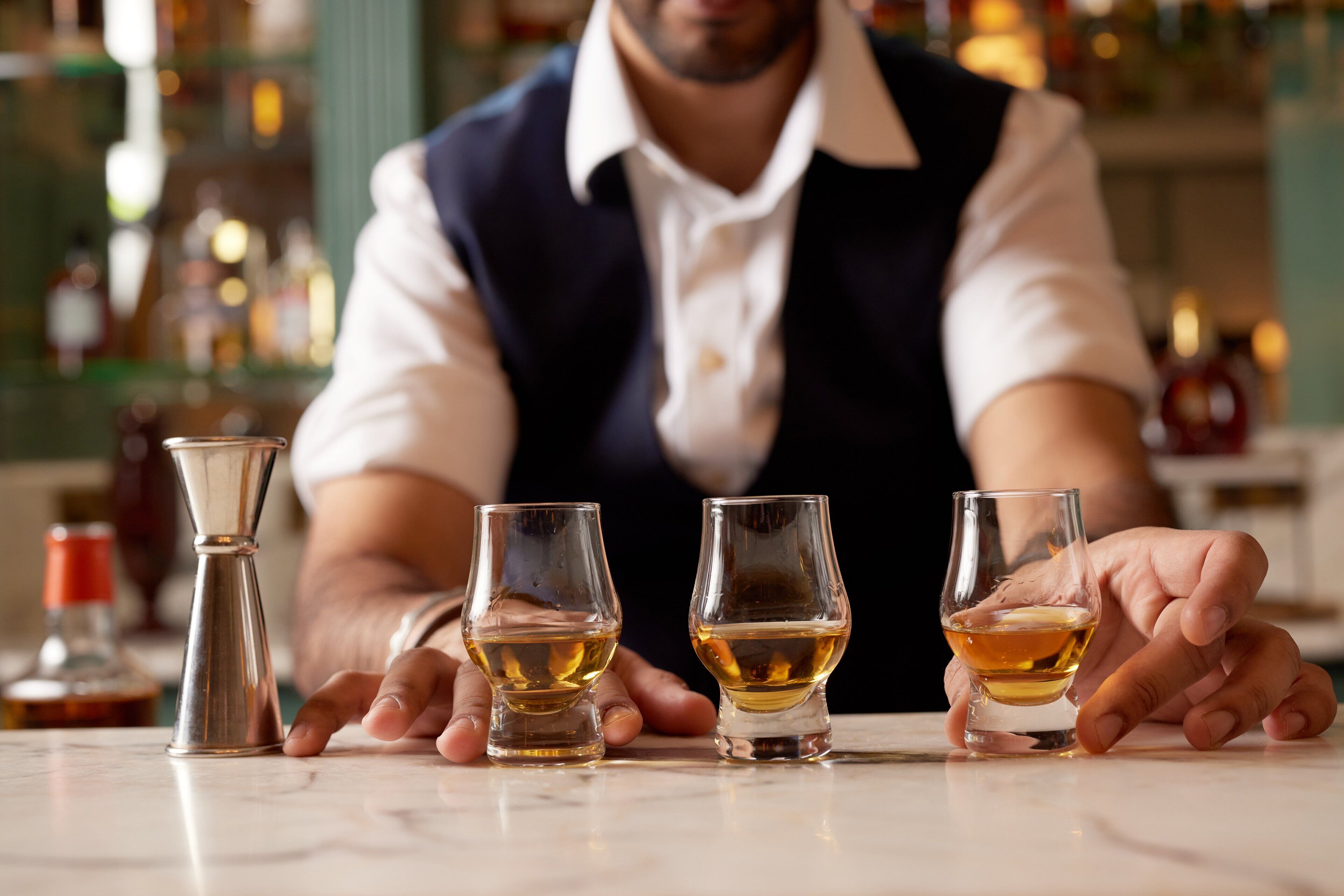 A bar setting with a bartender and three shot glasses on a marble countertop.
