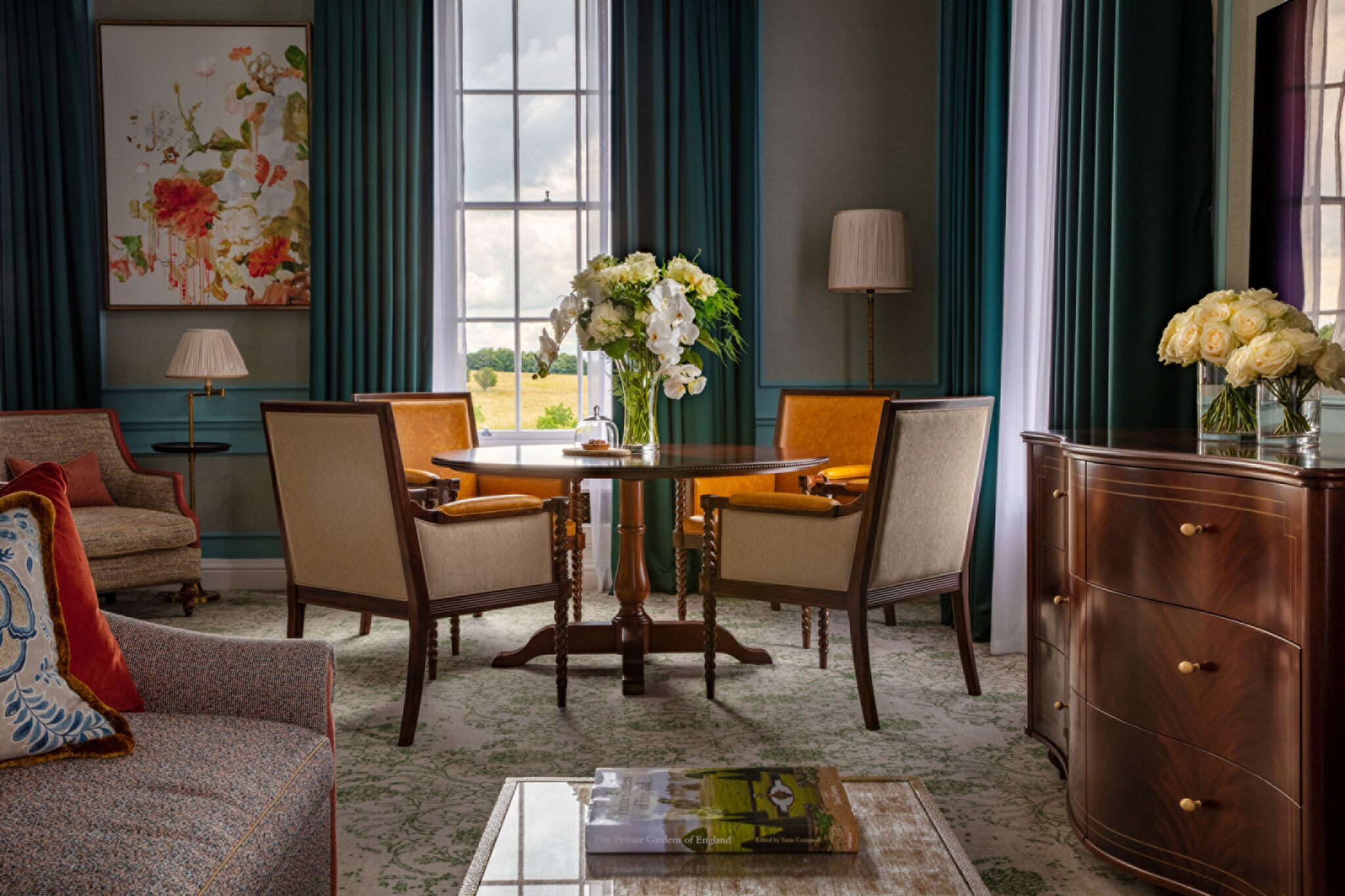 A room with a round table, two chairs, a sofa, a cabinet, and a painting on the wall.