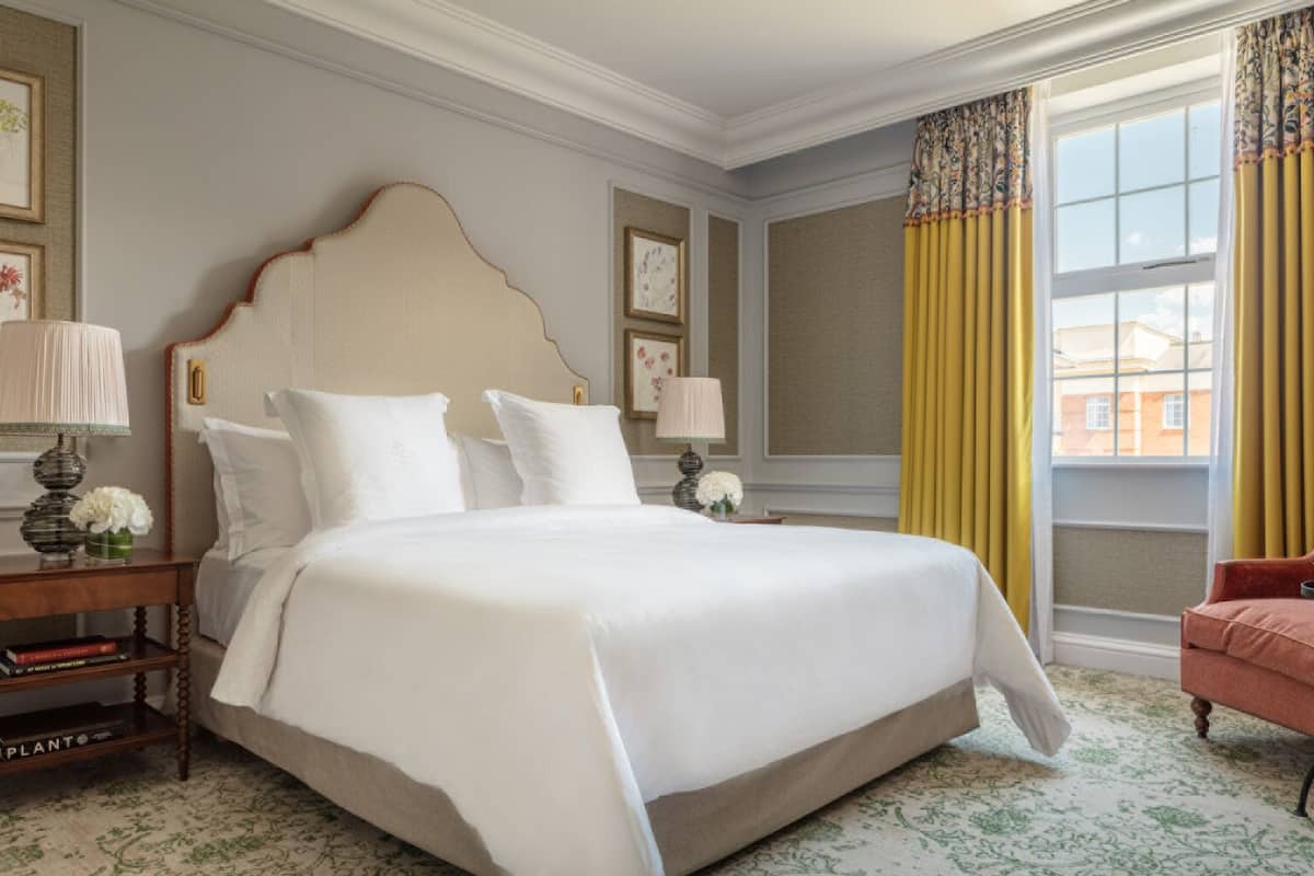 A hotel room with a large bed, two bedside tables, a chair, and a window with curtains.