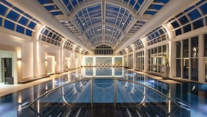 A large indoor swimming pool with a glass ceiling, surrounded by walls with windows and doors. - Four Seasons Hotel Hampshire (Hook)