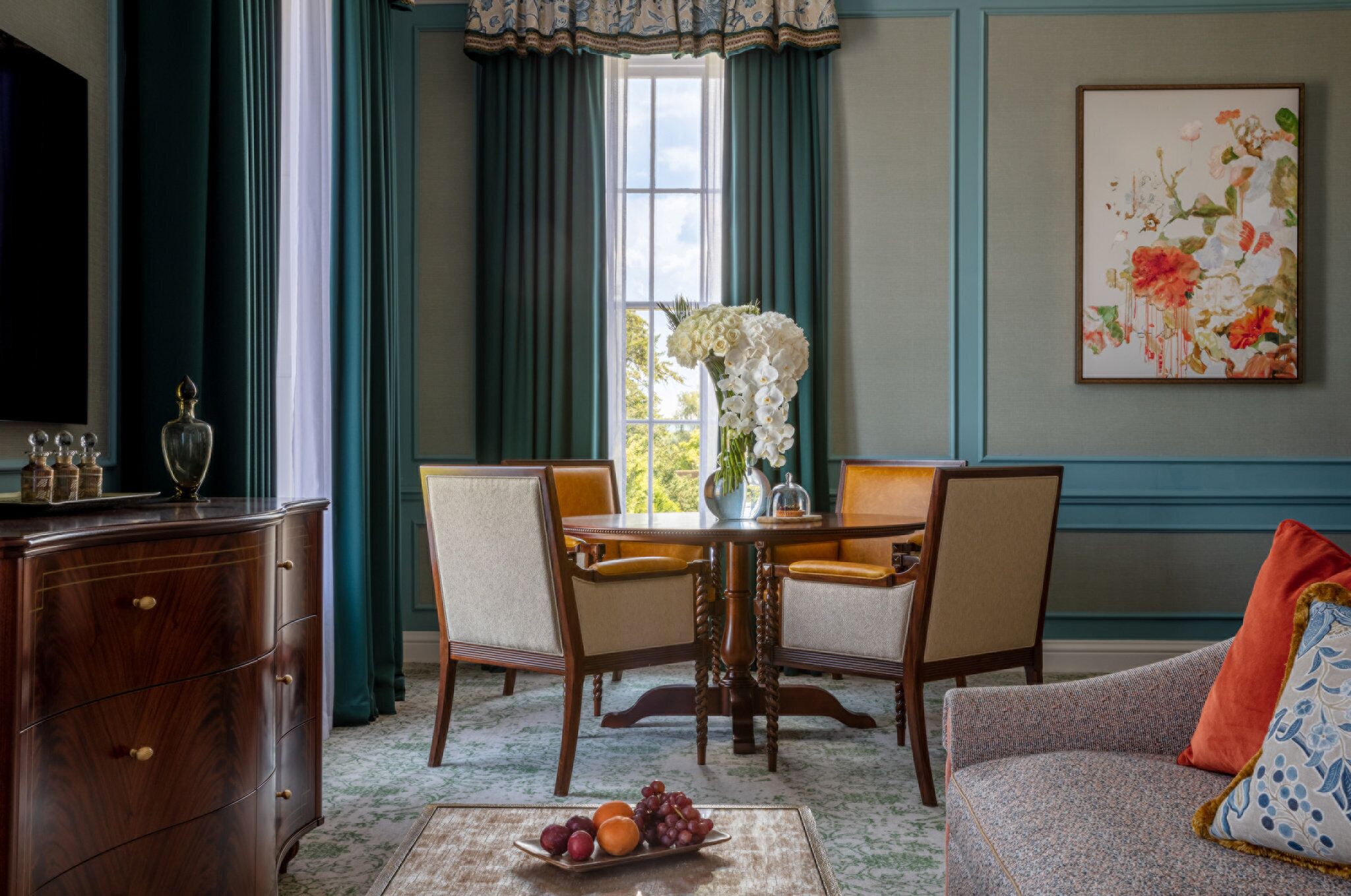 A dining area with a wooden table and chairs, a vase with flowers, and a fruit bowl on the table.