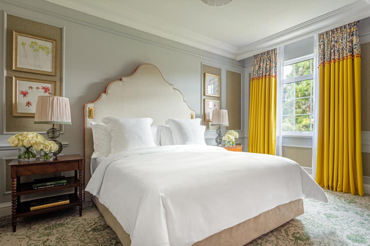 A spacious bedroom with a large bed, two bedside tables with lamps, and a window with yellow curtains.