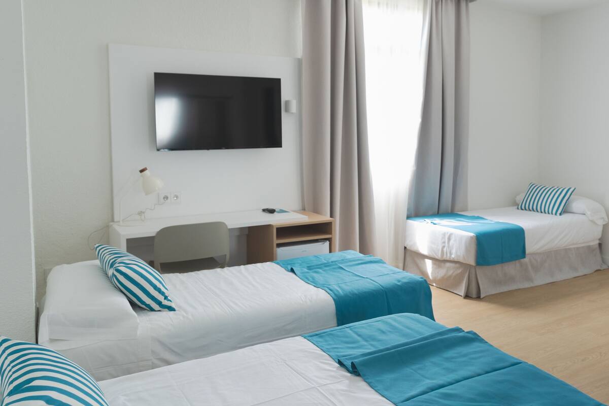 A hotel room with two beds, a desk, a chair, a TV, and a window with curtains.