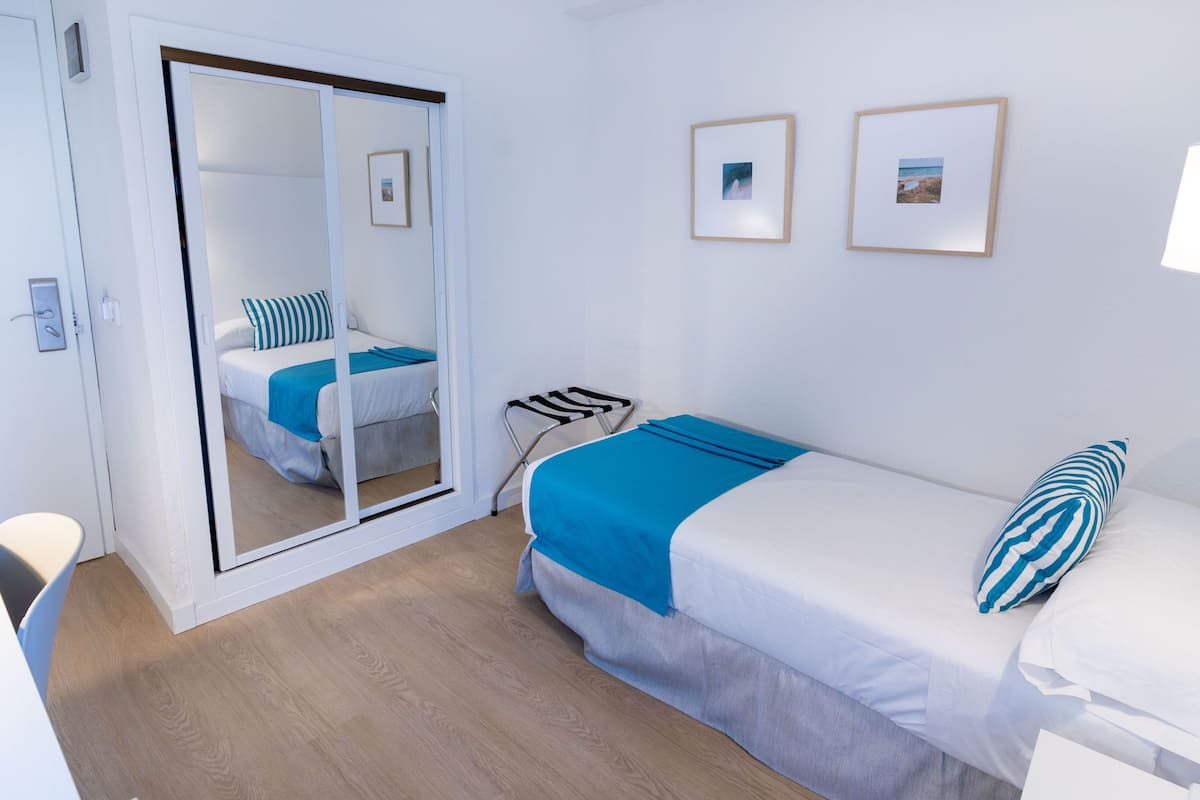 A bedroom with a bed, a chair, a desk, a mirror, and two framed pictures on the wall.