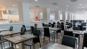 A spacious dining area with multiple tables and chairs, a kitchen area in the background, and a clean, modern design. - BLUESEA Costa Serena (Torremolinos)