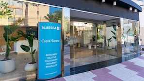 A hotel entrance with a reception desk, indoor seating area, and a glass facade reflecting the surroundings. - BLUESEA Costa Serena (Torremolinos)