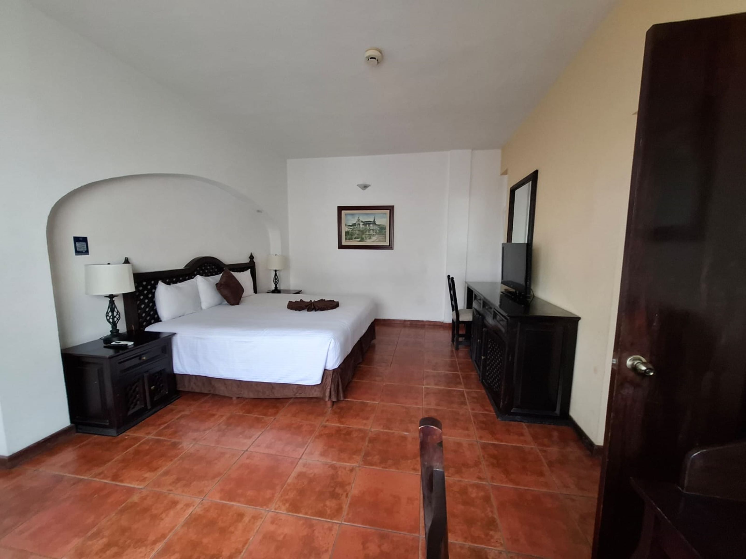 Una habitación de hotel con cama, escritorio con televisor, silla y puerta.
