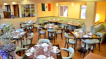 A restaurant with multiple dining tables and chairs, a flag on the wall, and a counter area.