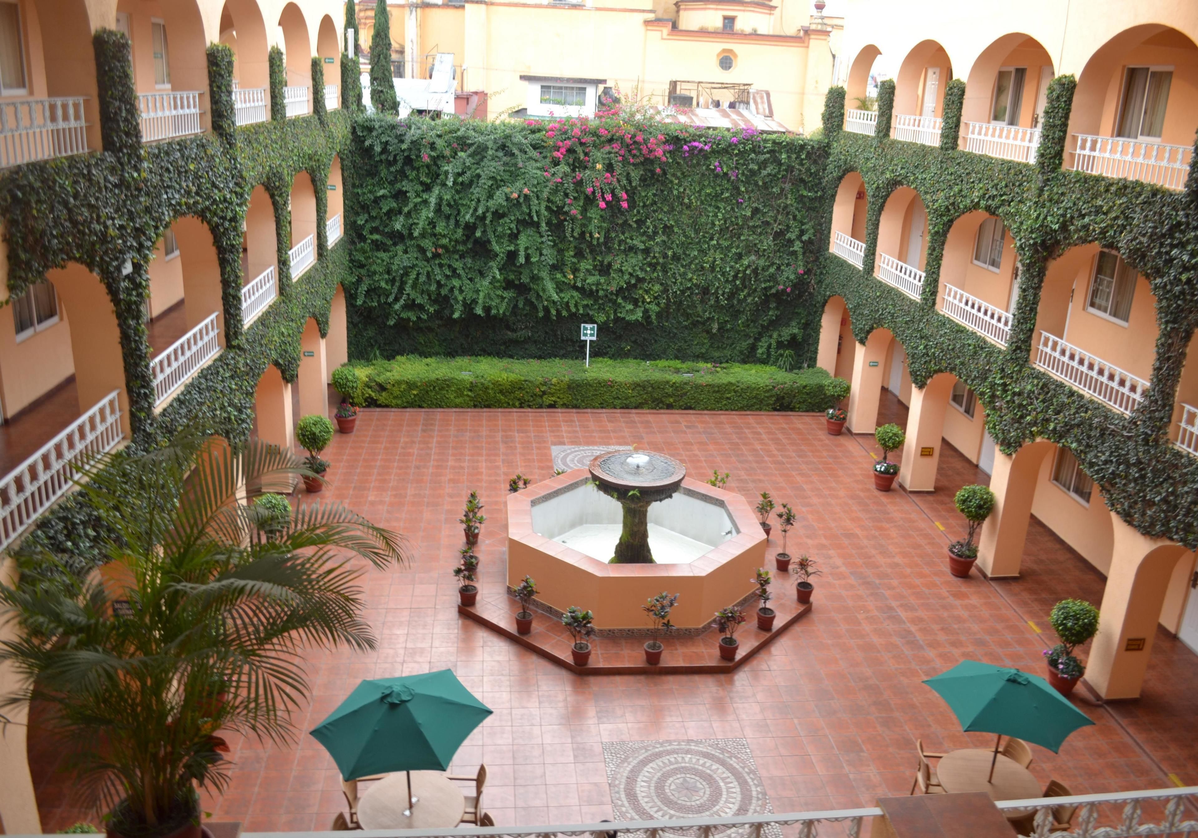 A courtyard with a central fountain, surrounded by potted plants and umbrellas.