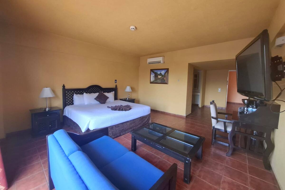 Ein Hotelzimmer mit Bett, Sofa, Couchtisch, Fernseher und Schreibtisch.