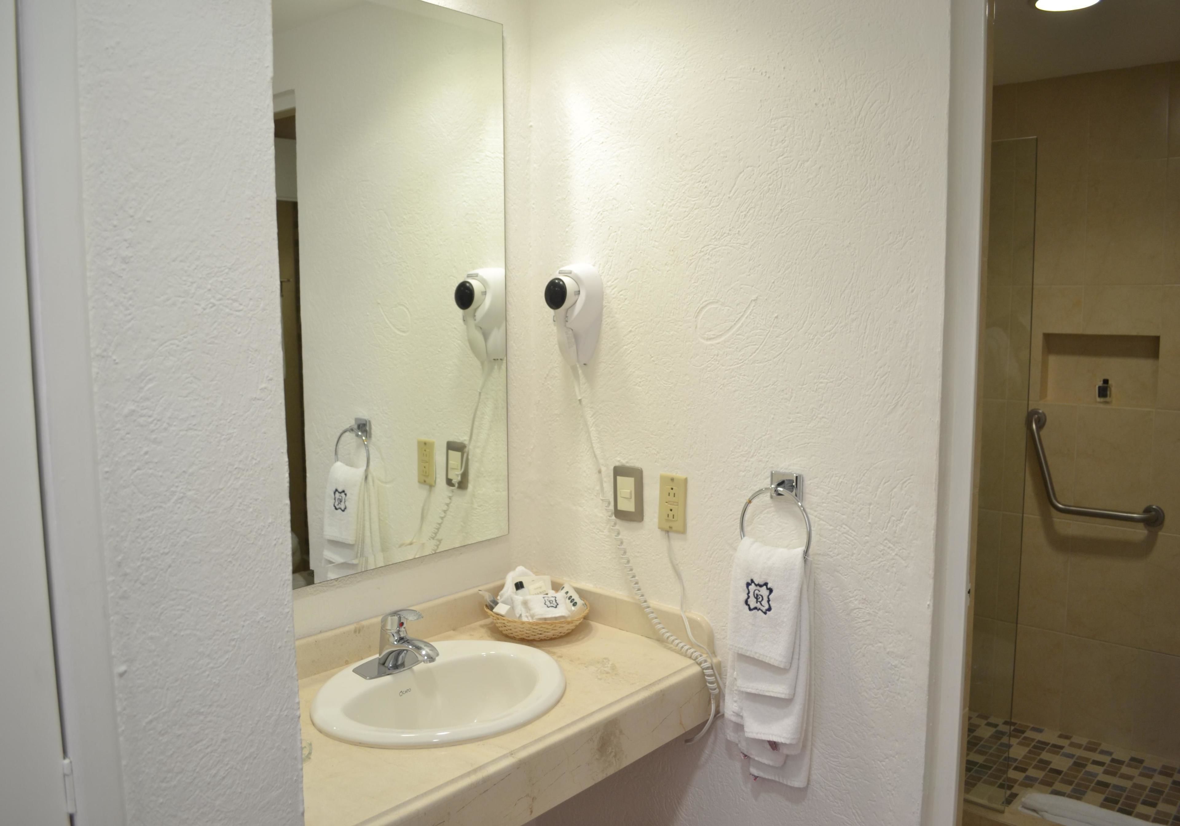A bathroom with a sink, mirror, hair dryer, towel rack, and a shower area.