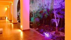 A corridor with tiled flooring, a bench, and a wall with a large, illuminated mural of tropical plants. - Hotel Misión Orizaba (Orizaba)