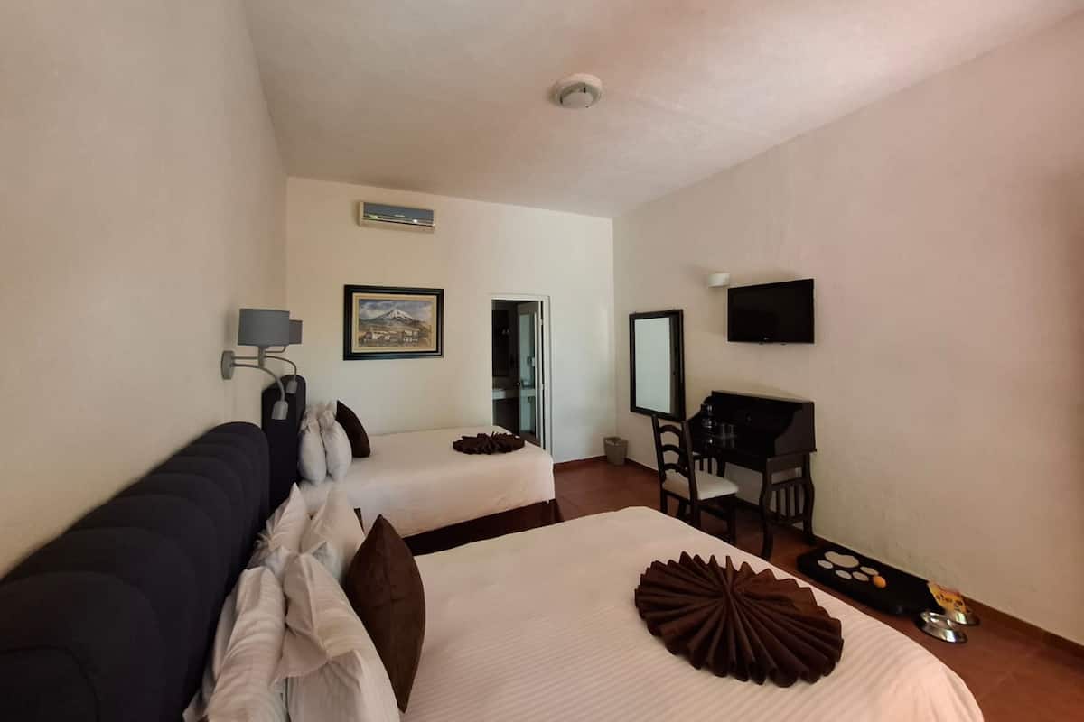 Ein Hotelzimmer mit zwei Betten, einem Schreibtisch, einem Stuhl, einem Fernseher und einem gerahmten Bild an der Wand.