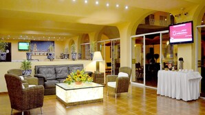 A hotel lobby with a reception desk, seating area with chairs and a sofa, a coffee table with flowers, and a television screen displaying a welcome message. - Hotel Misión Orizaba (Orizaba)