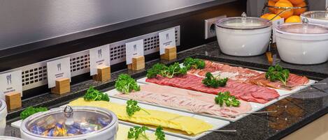 A buffet with various food options including meats, cheeses, and a selection of fruits.