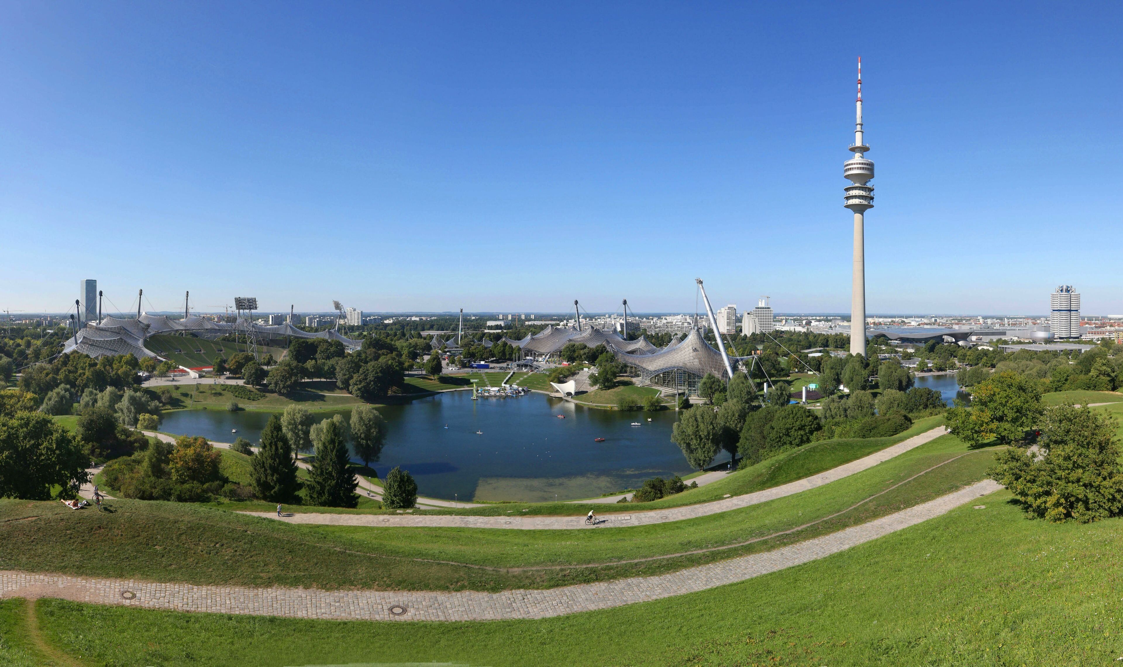 Vista panorámica de una ciudad con una torre destacada, un lago y un parque con senderos.