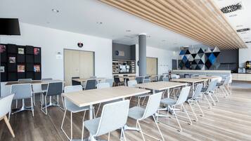 A modern dining area with multiple tables and chairs, a kitchen area, and a wall with geometric patterns.