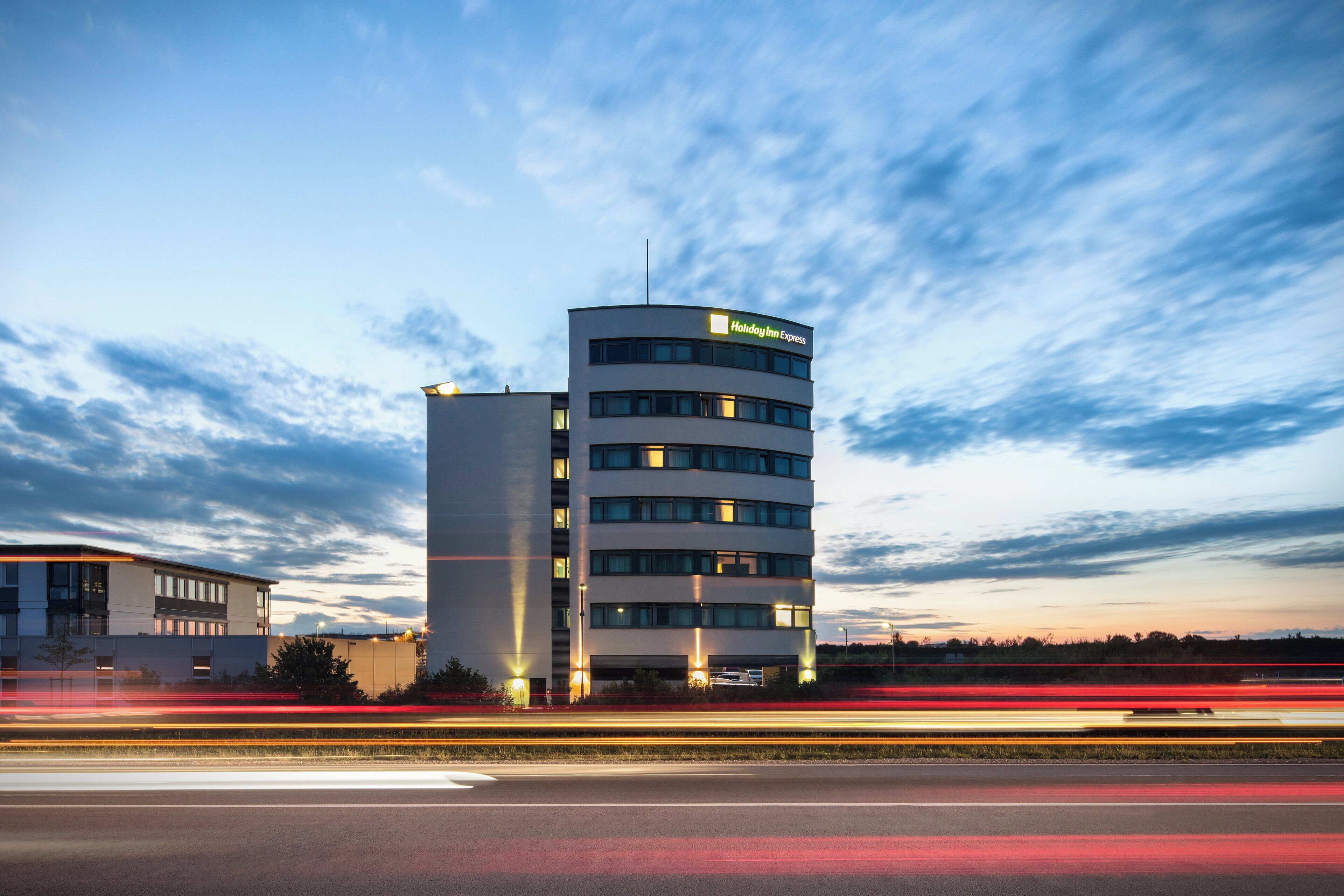 Een meerlaags Holiday Inn Express gebouw met een modern architectonisch ontwerp, met een opvallende gebogen hoek en een plat dak.