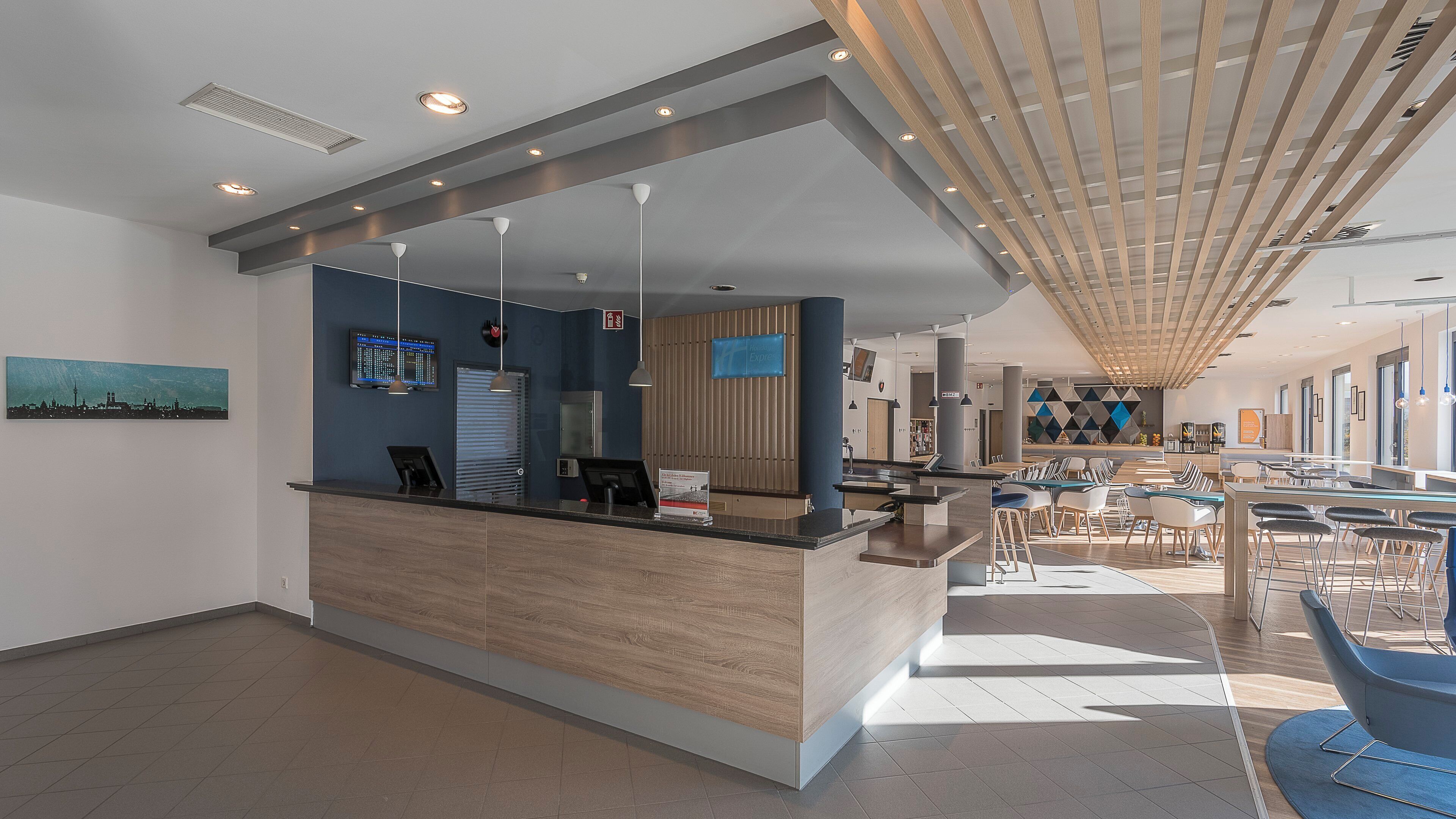 A modern hotel lobby with a reception desk, seating area, and a large digital display.