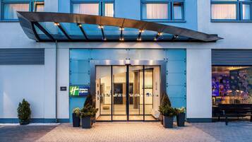 A Holiday Inn Express hotel entrance with a glass door, potted plants, and a blue awning.