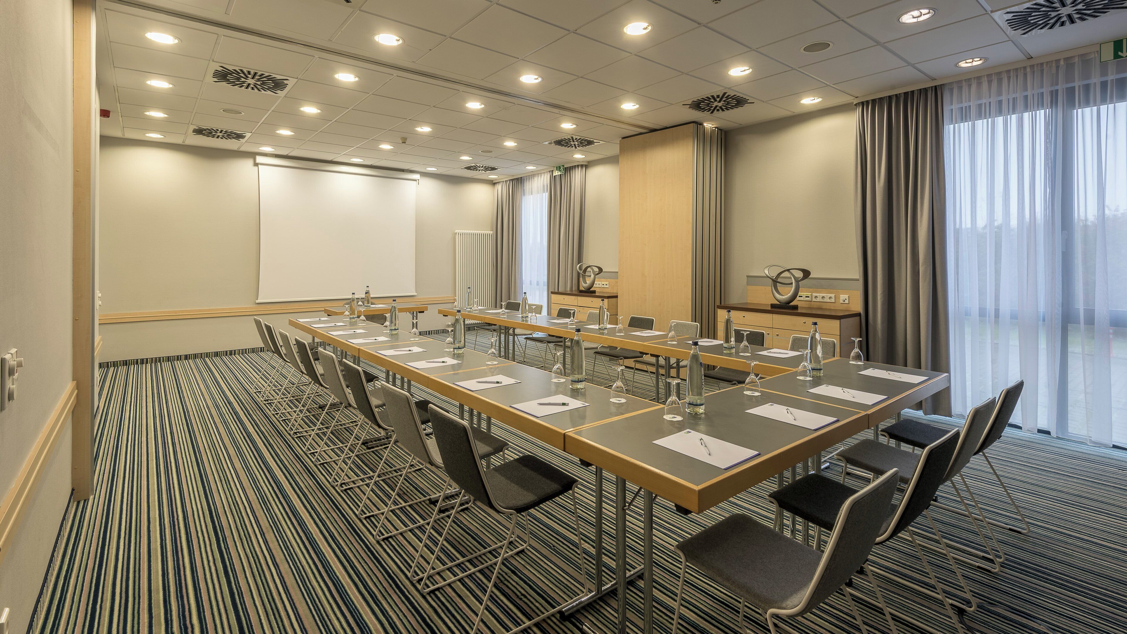 A conference room with a long table, chairs, and a projector screen.