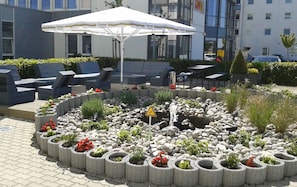 An outdoor seating area with planters and a yellow warning sign. - Holiday Inn Express München-Messe by IHG (Feldkirchen)