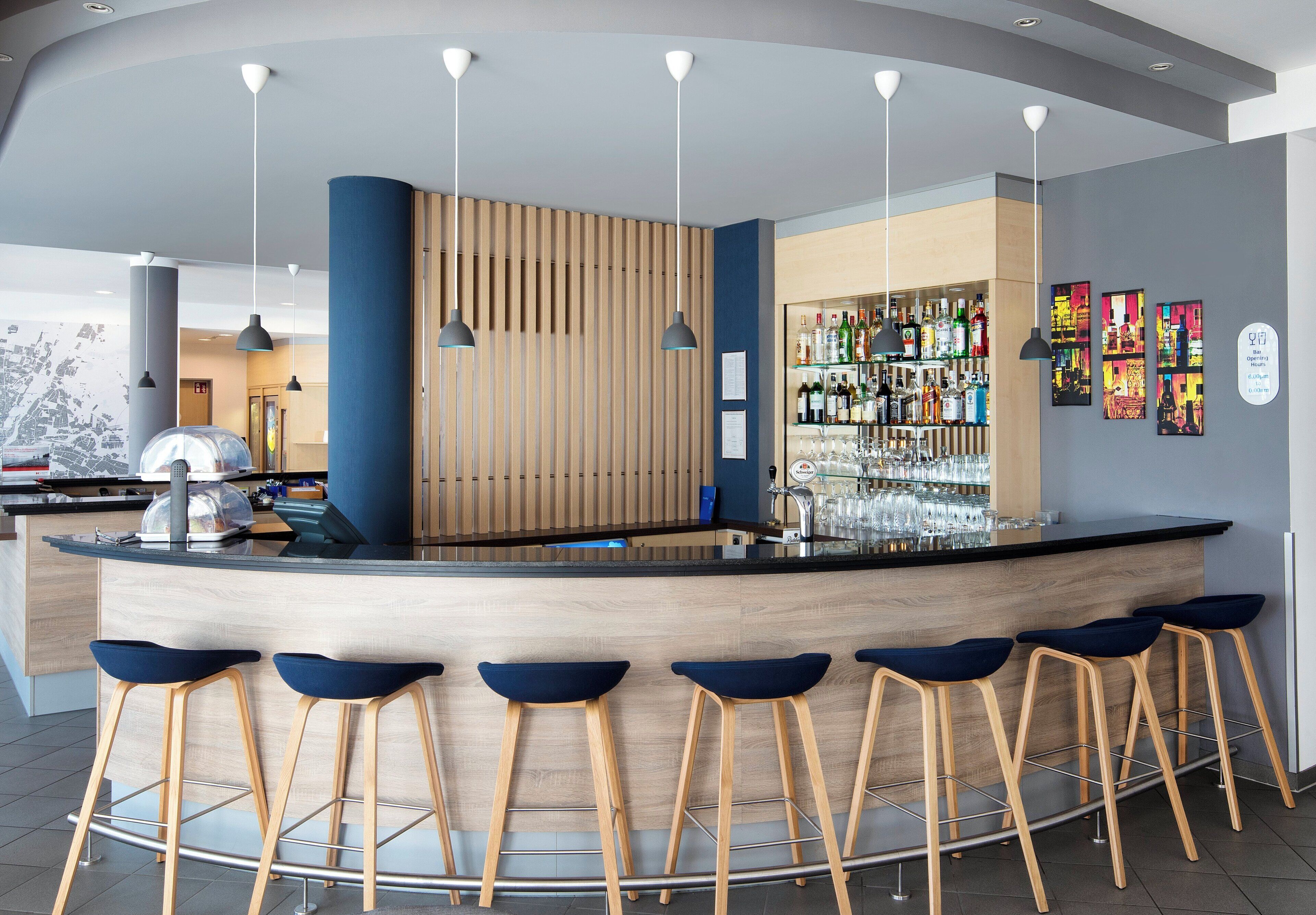 A modern bar area with a curved counter, wooden stools, and a variety of bottles and glasses.