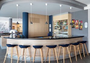 A modern bar area with a curved counter, wooden stools, and a variety of bottles and glasses. - Holiday Inn Express München-Messe by IHG (Feldkirchen)