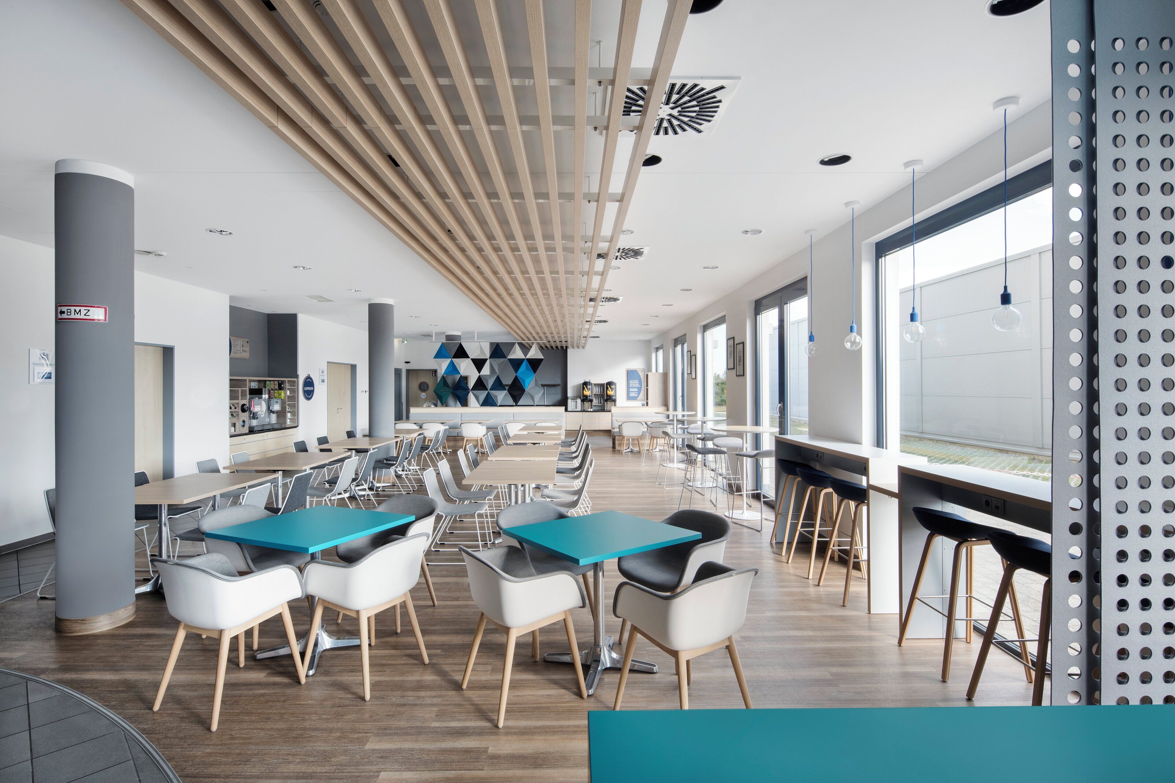A modern cafeteria with long tables, chairs, and a high ceiling with wooden slats.