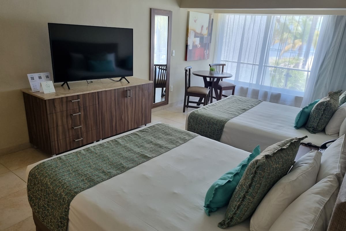 A hotel room with two beds, a TV, a wooden cabinet, a dining table, and a window with curtains.