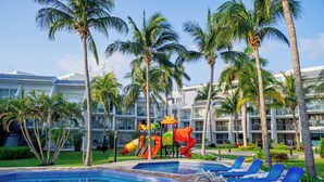 A swimming pool with lounge chairs, palm trees, and a children's play area with slides. - Ocean Spa Hotel – All Inclusive (Cancun)