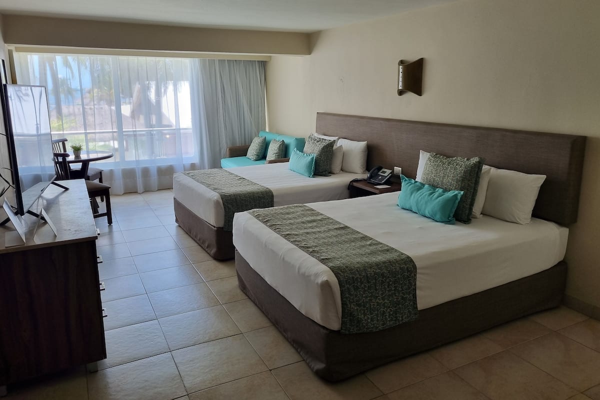 A hotel room with two beds, a desk, and a view of the outdoors.