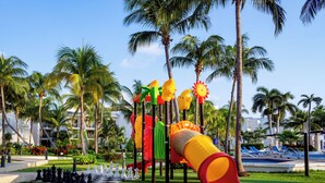 A playground with slides and climbing structures, surrounded by palm trees and a pool area. - Ocean Spa Hotel – All Inclusive (Cancun)