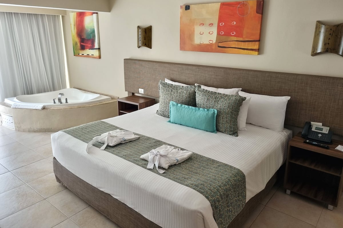 A hotel room with a large bed, a separate bathtub, a bedside table with a phone, and a painting on the wall.